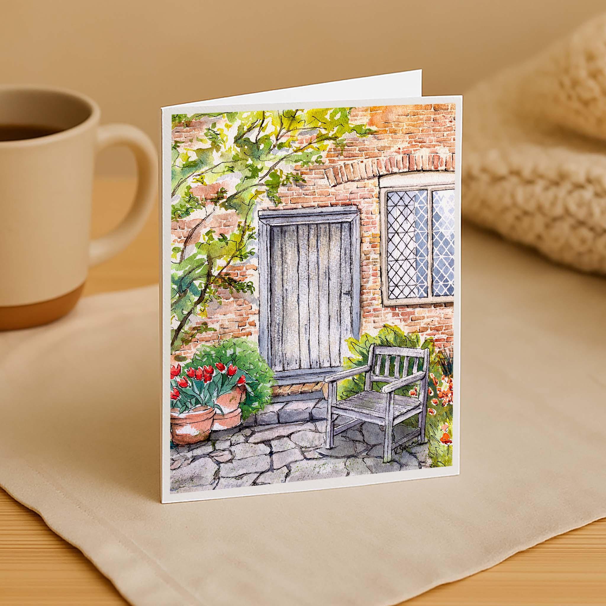 Greeting card with garden scene on a table with a mug and knitted item.