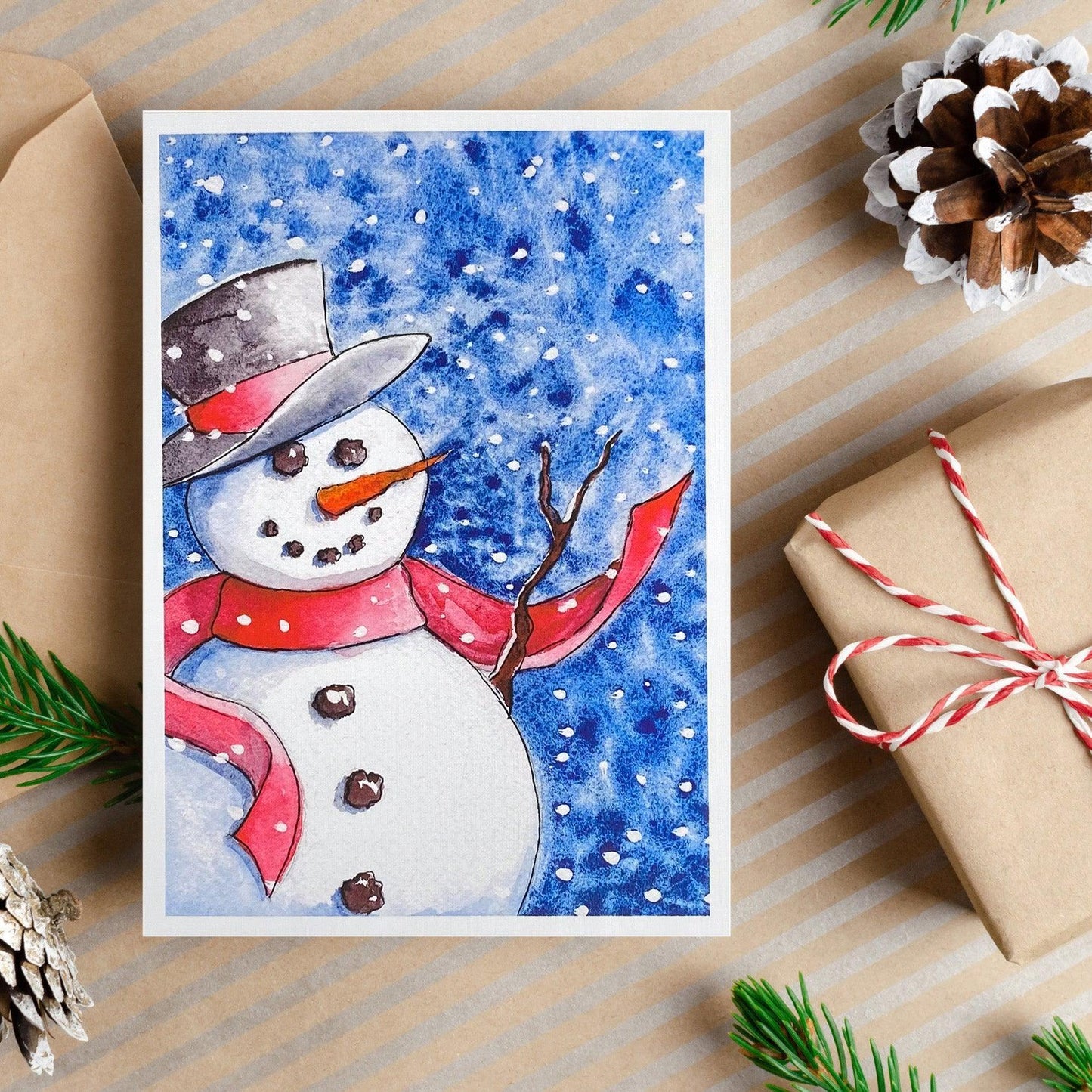 A watercolor painting of a snowman wearing a red scarf and black top hat with snow falling against a deep blue sky.
