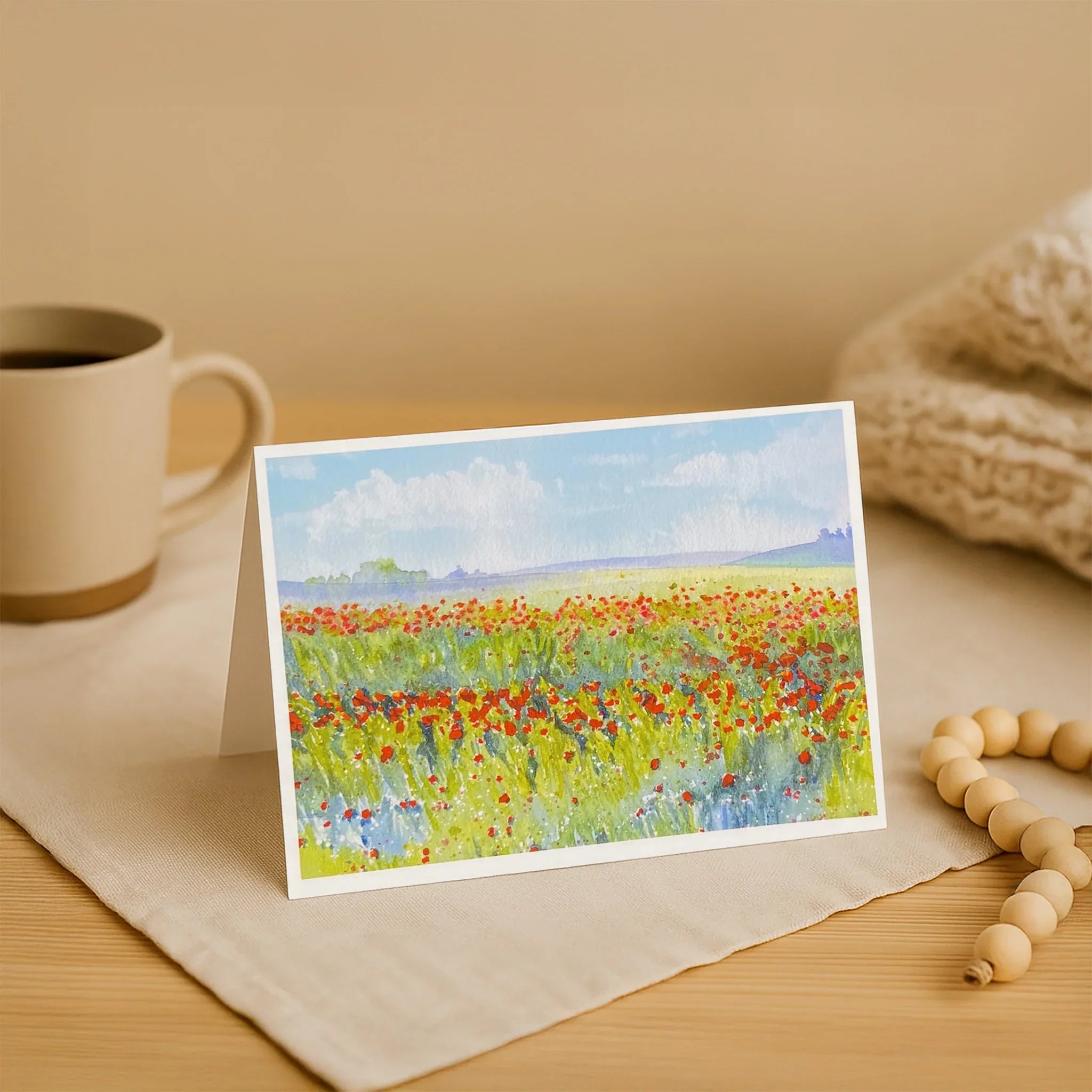 Note card with a floral landscape design on a wooden surface with a mug and beads.