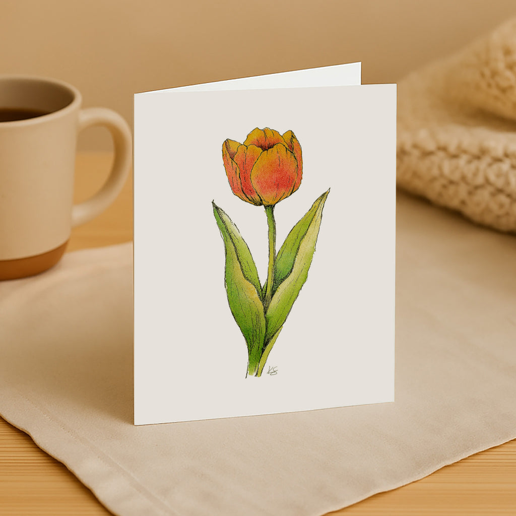 Greeting card with a tulip illustration on a beige surface with a mug and woven item.