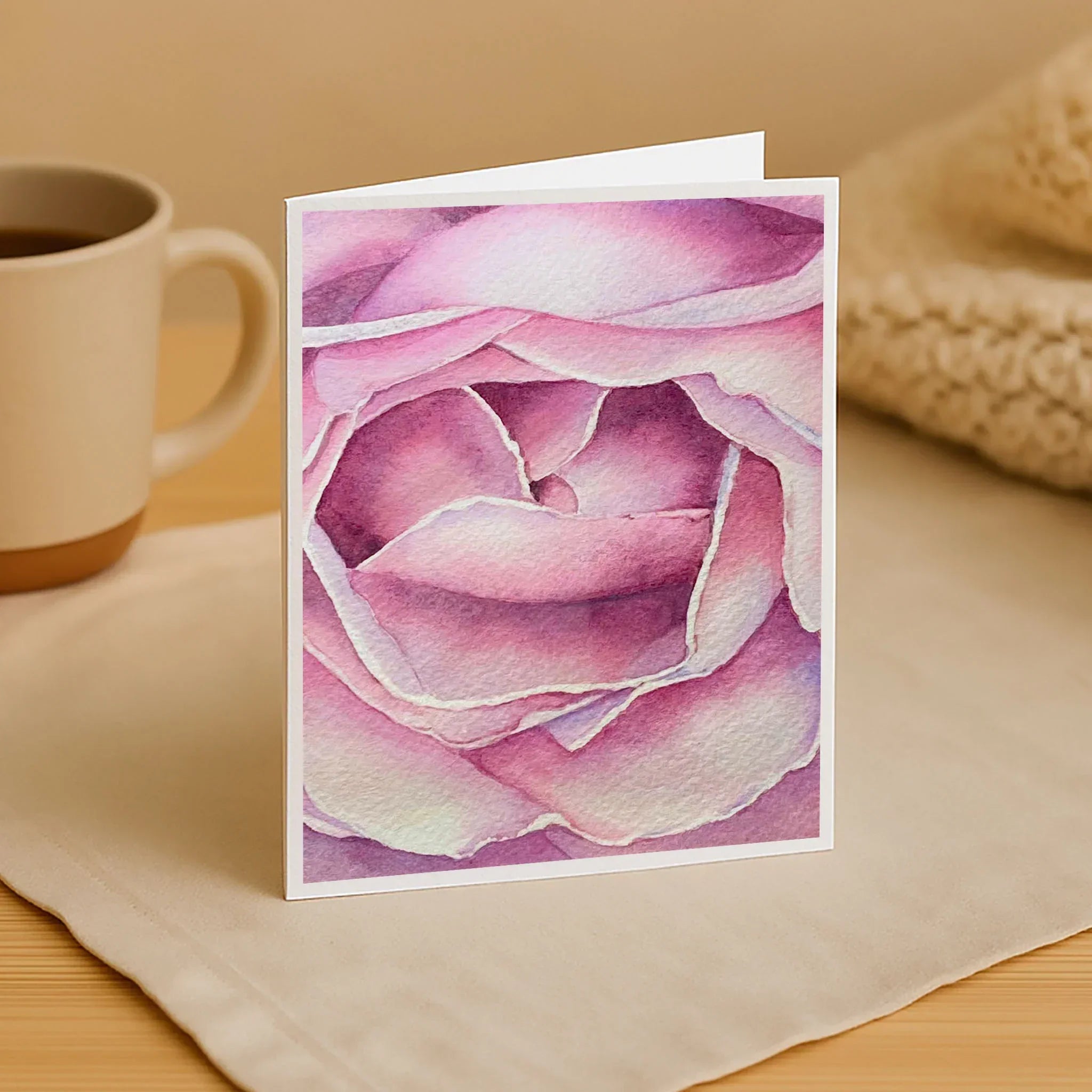 Card with pink rose design on a table with a mug and fabric