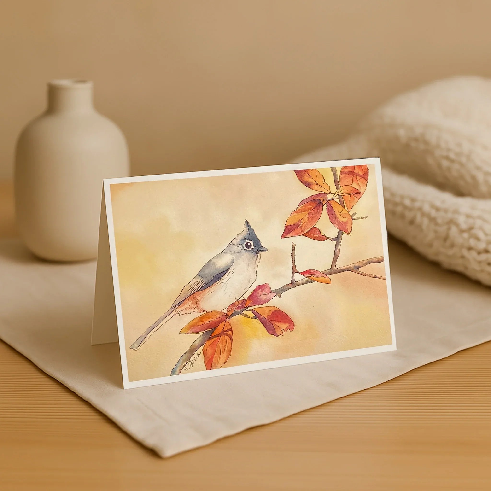Greeting card with a bird and autumn leaves design on a beige surface.