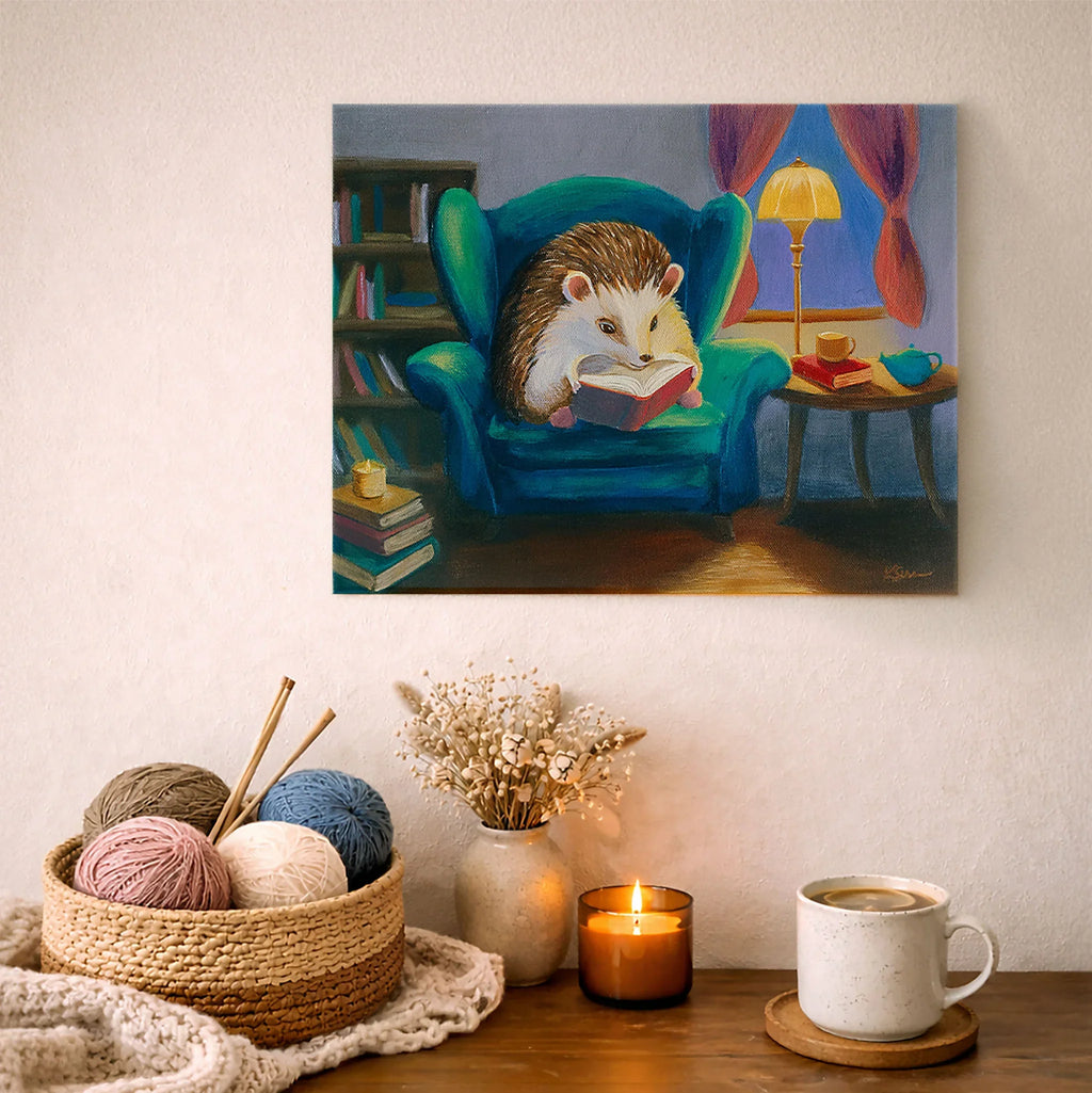 Painting of a hedgehog reading a book on an armchair, displayed above a cozy table setting with yarn, a mug, and a candle.