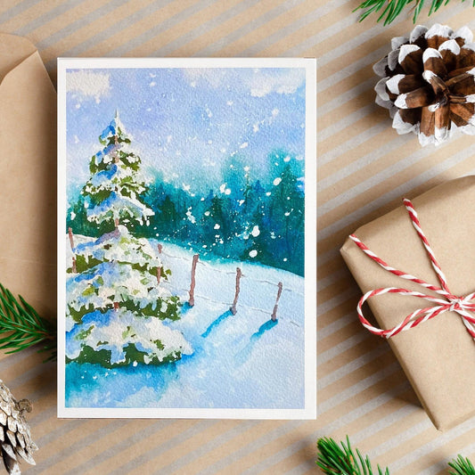 A watercolor painting of a snow-covered evergreen tree beside a wooden fence, with soft snowfall against a blue sky and distant forest.