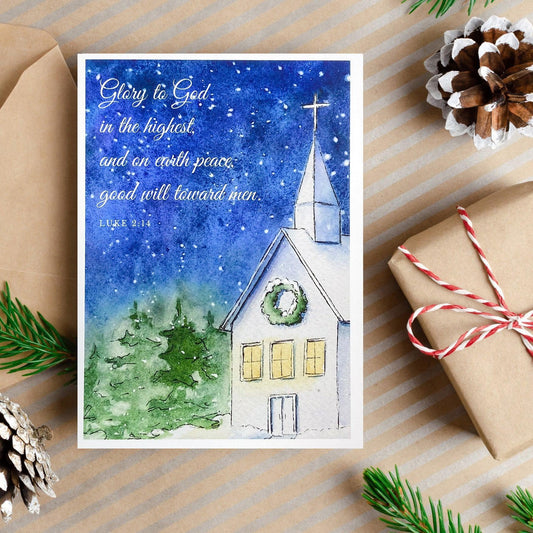 A watercolor and ink painting of a church at night with a wreath on the front and the Bible verse Luke 2:14 written in white text across a deep blue snowy sky.